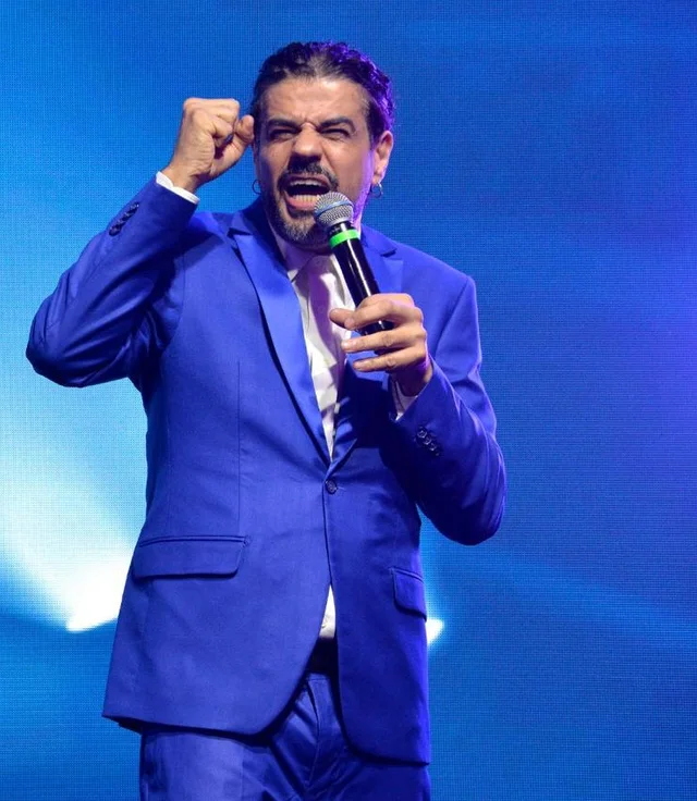 Alexandre Camilo palestrando de terno azul, com microfone na mão